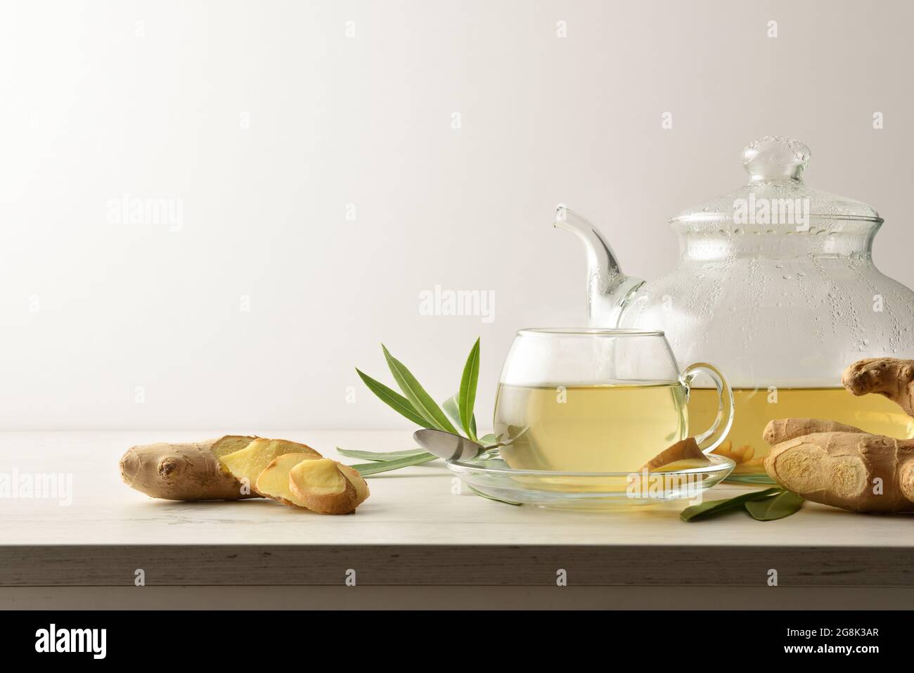 Tazza calda di zenzero su un tavolo di legno con radice di zenzero, teiera e foglie con sfondo bianco isolato. Vista frontale. Foto Stock