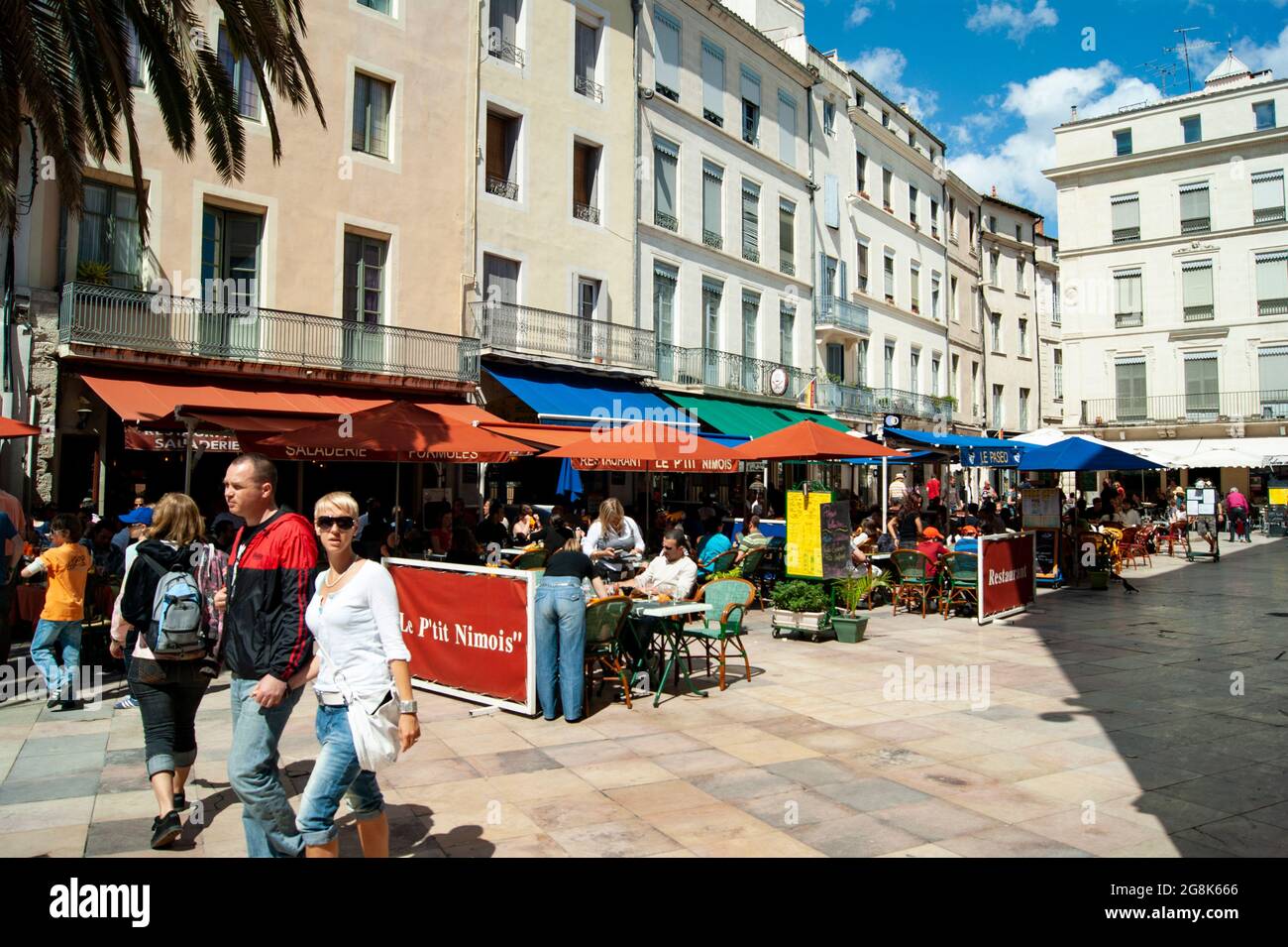 Nimes, France Place de Marche i ristoranti e le caffetterie lungo una piazza colorata in questa storica città del sud della Francia la gente gode del paesaggio e Foto Stock