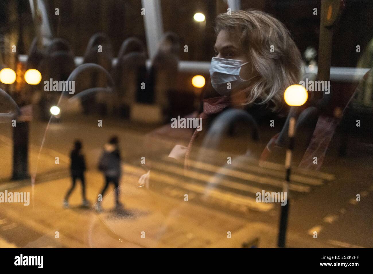Ragazza bionda che indossa la maschera facciale riflessa nella finestra degli autobus di notte, Londra, 21 febbraio 2021 Foto Stock