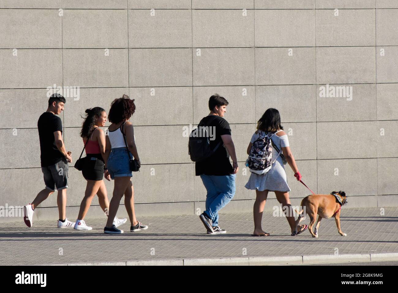Gruppo di giovani che camminano vicino a una parete grigia. Foto Stock