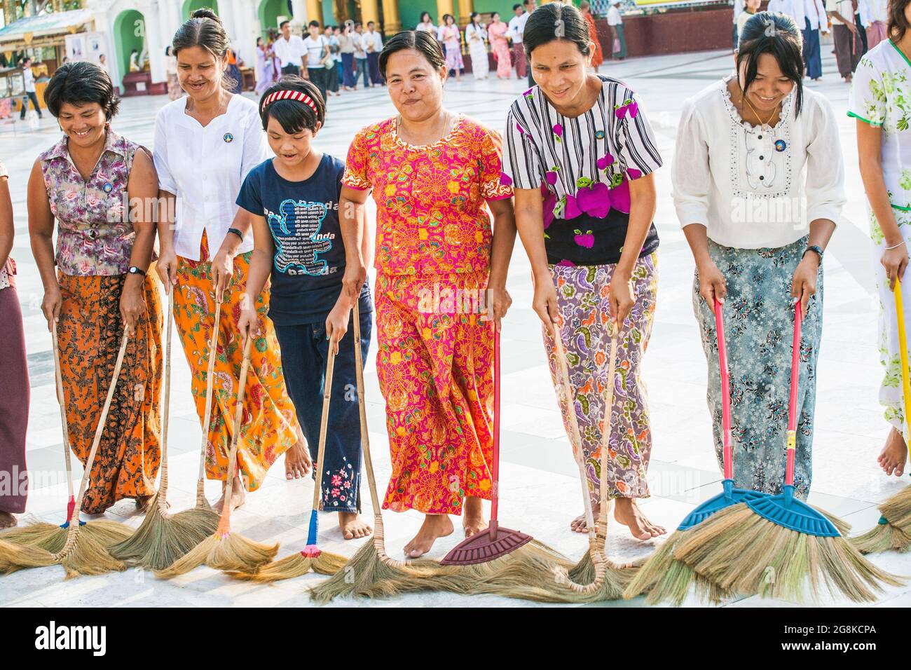 Fila di Signore birmani che spazzano pavimento in marmo all'unisono con scopa a Shwedagon Pagoda per guadagnare merito o credito spirituale, Yangon, Myanmar Foto Stock