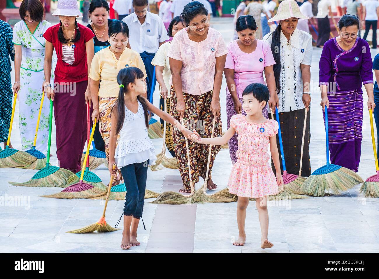 Fila di donne e bambini birmani che spazzano il pavimento di marmo all'unisono con scopa a Shwedagon Pagoda per guadagnare merito o credito spirituale, Yangon, Myanmar Foto Stock