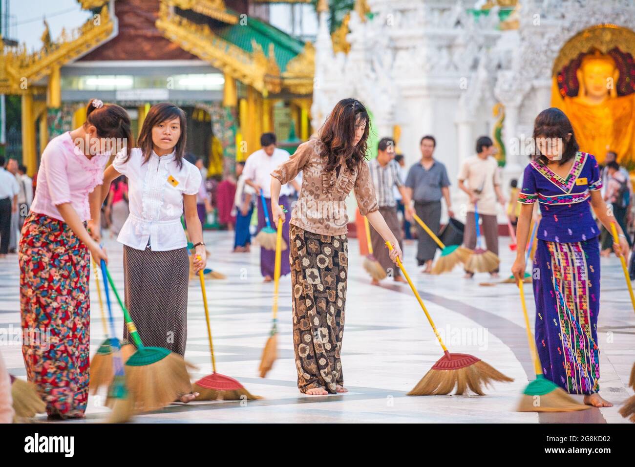 Fila di belle Signore birmani spazzare pavimento in marmo all'unisono con scopa a Shwedagon Pagoda per guadagnare merito o credito spirituale, Yangon, Myanmar Foto Stock