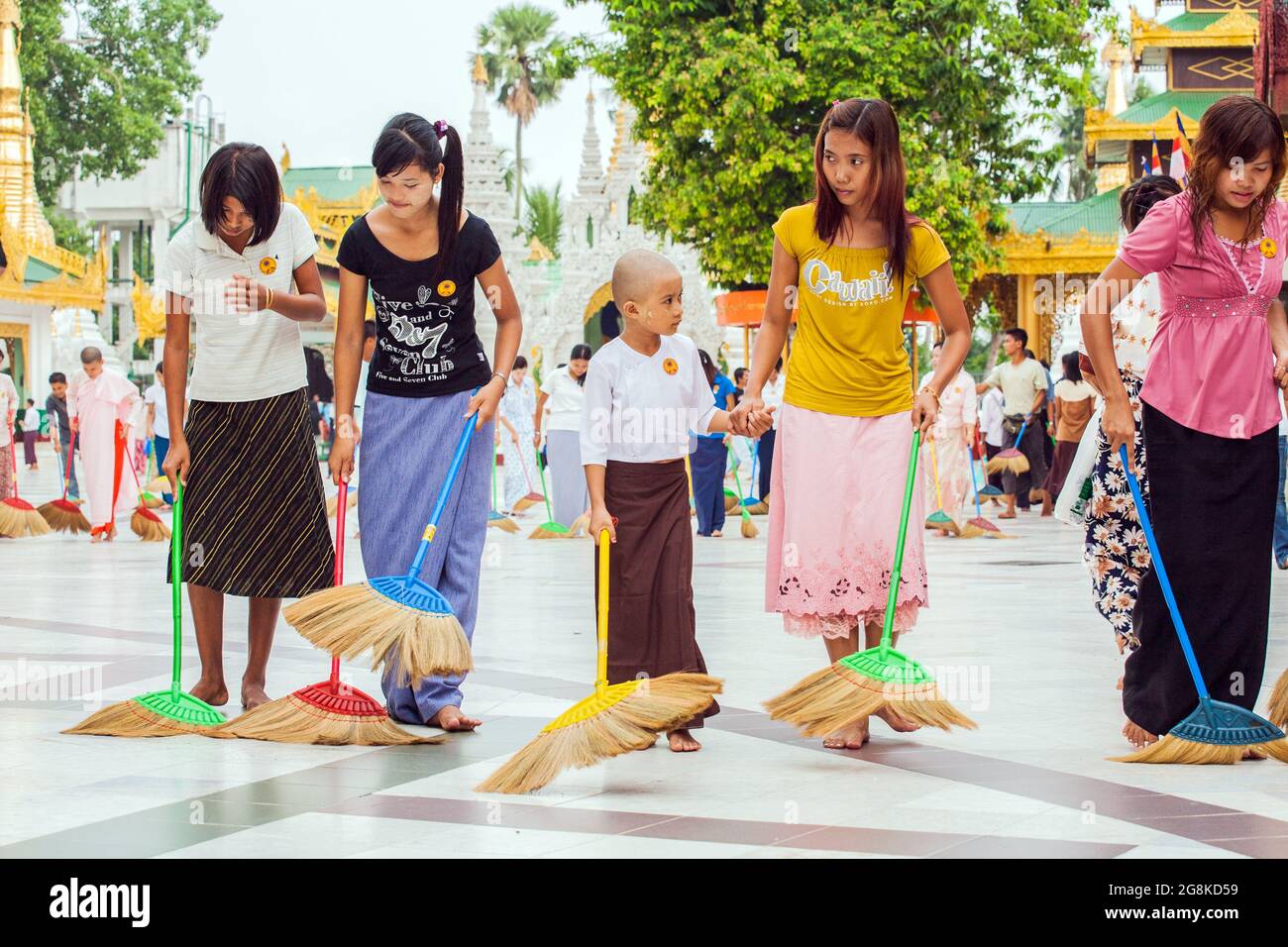 Fila di belle ragazze birmane spazzare pavimento in marmo all'unisono con scopa a Shwedagon Pagoda per guadagnare merito o credito spirituale, Yangon, Myanmar Foto Stock