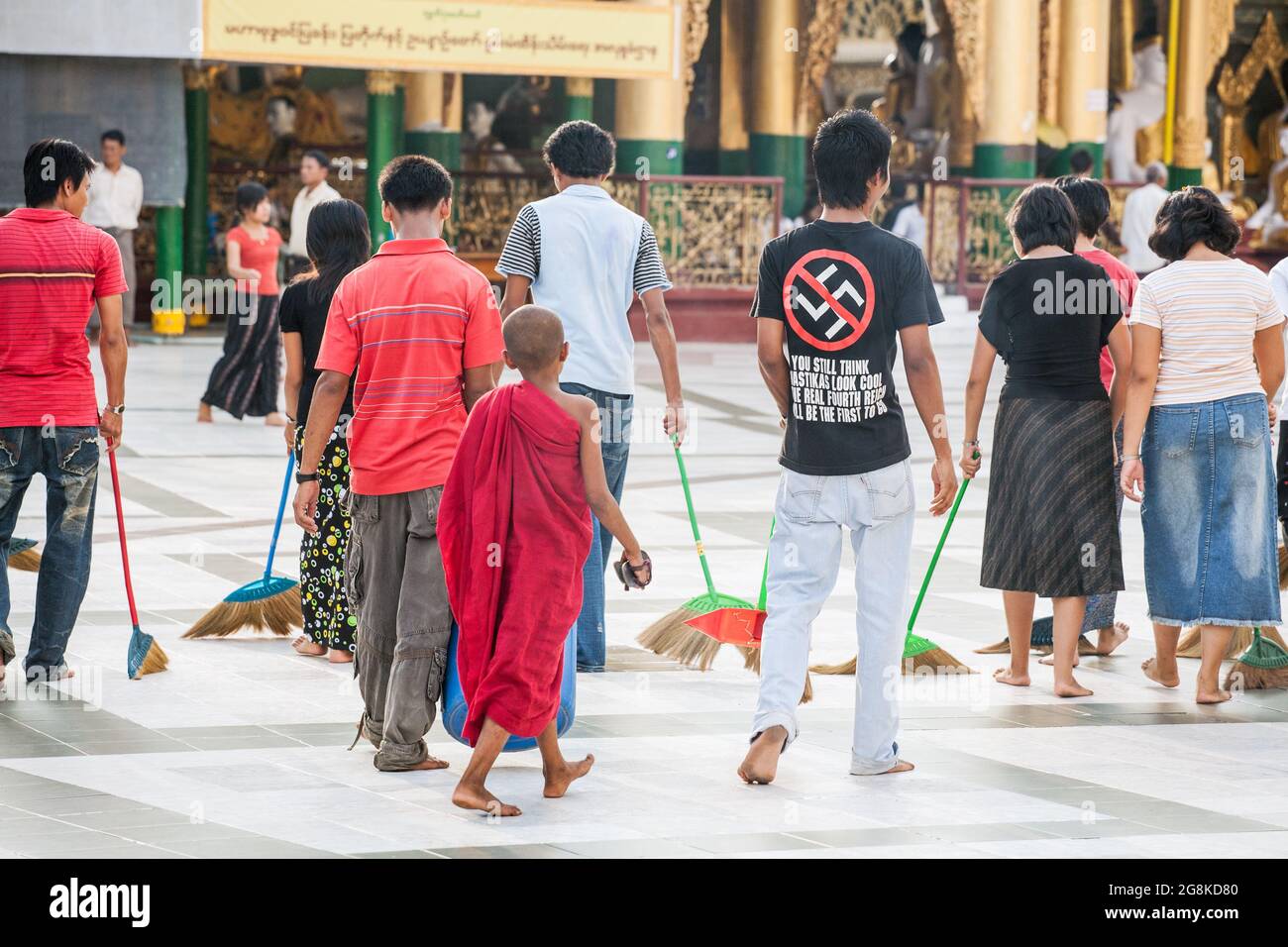 I birmani spazzano il pavimento in marmo all'unisono con le scopa alla Pagoda di Shwedagon per guadagnare merito seguito da giovani che indossano la t-shirt swastika, Yangon, Myanmar Foto Stock