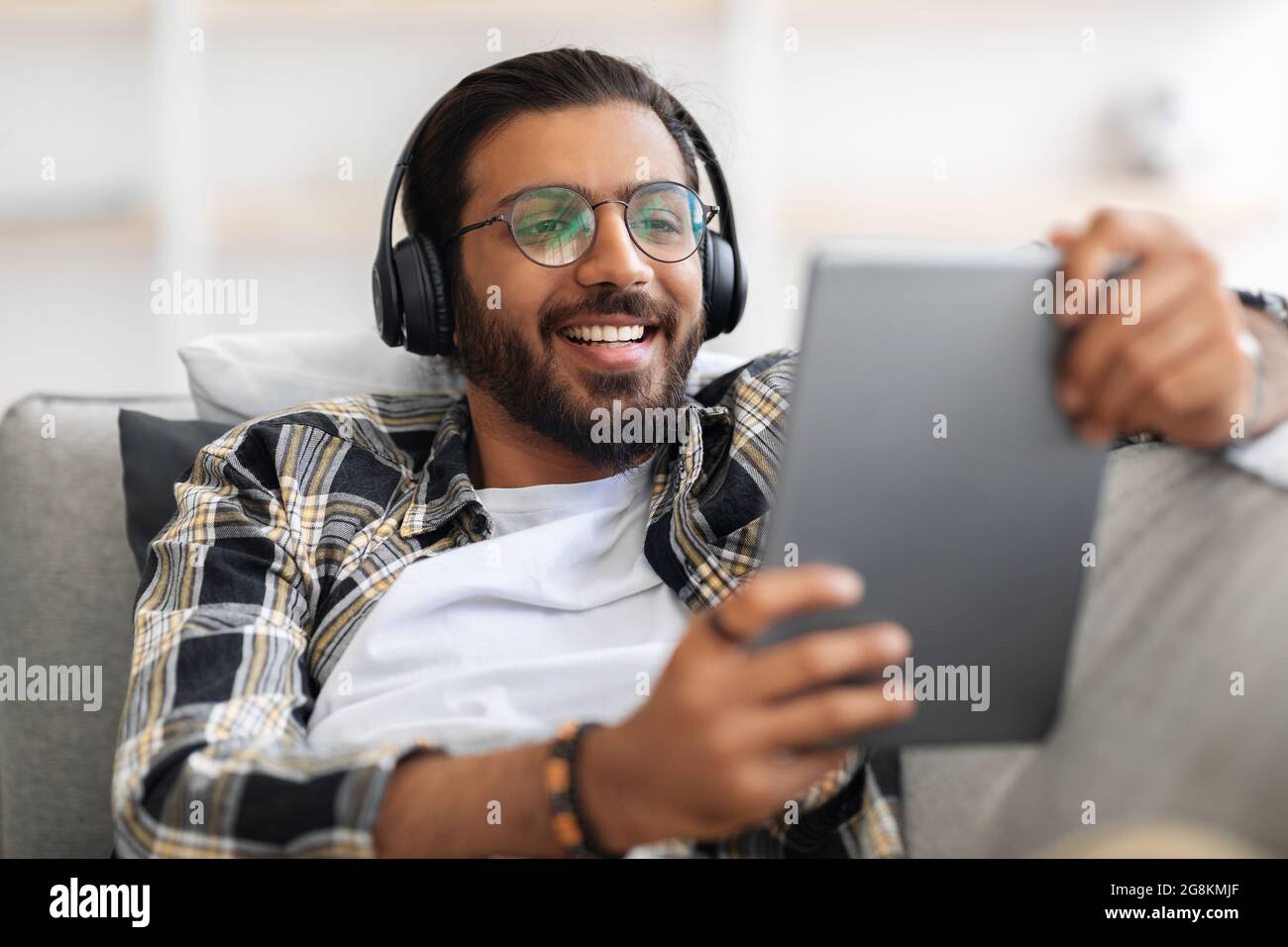 Gioioso ragazzo arabo che guarda i video su un tablet digitale a casa Foto Stock