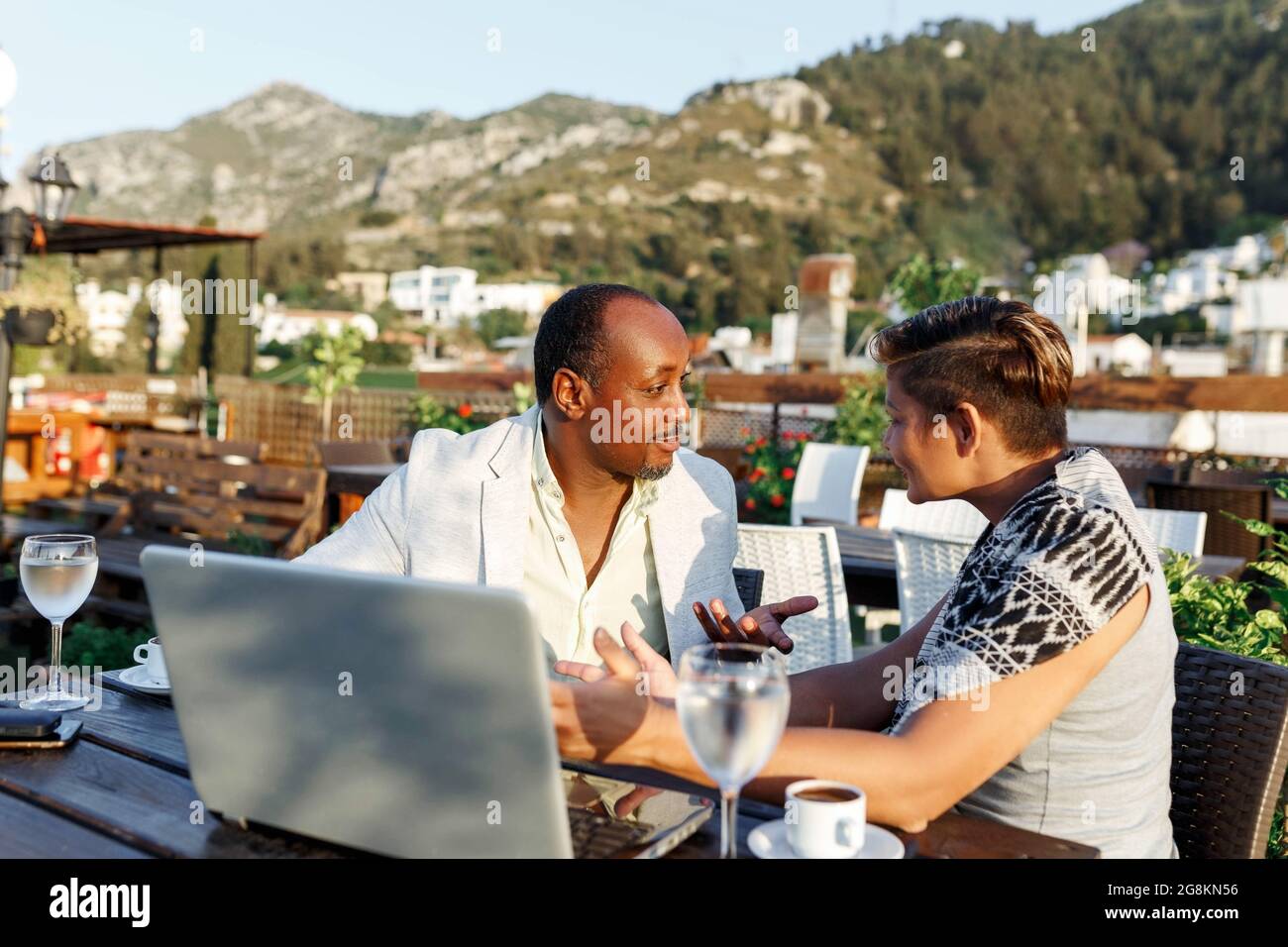 Coworking e freelance Concept.Mixed corsa, di media età pelle nera uomo e donna che lavorano insieme sul computer portatile mentre si siede sulla terrazza del caffè. Foto Stock