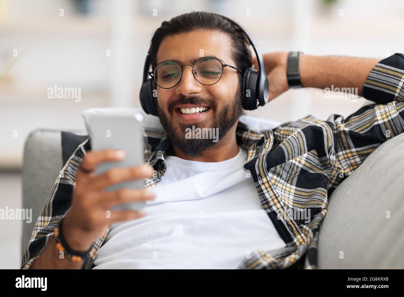 Allegro ragazzo arabo che guarda film, utilizzando cuffie wireless e cellulare Foto Stock
