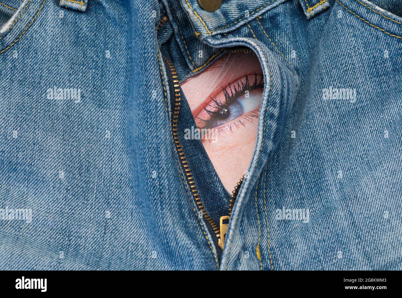 occhio femminile che guarda da dietro la cerniera aperta dei pantaloni in denim Foto Stock