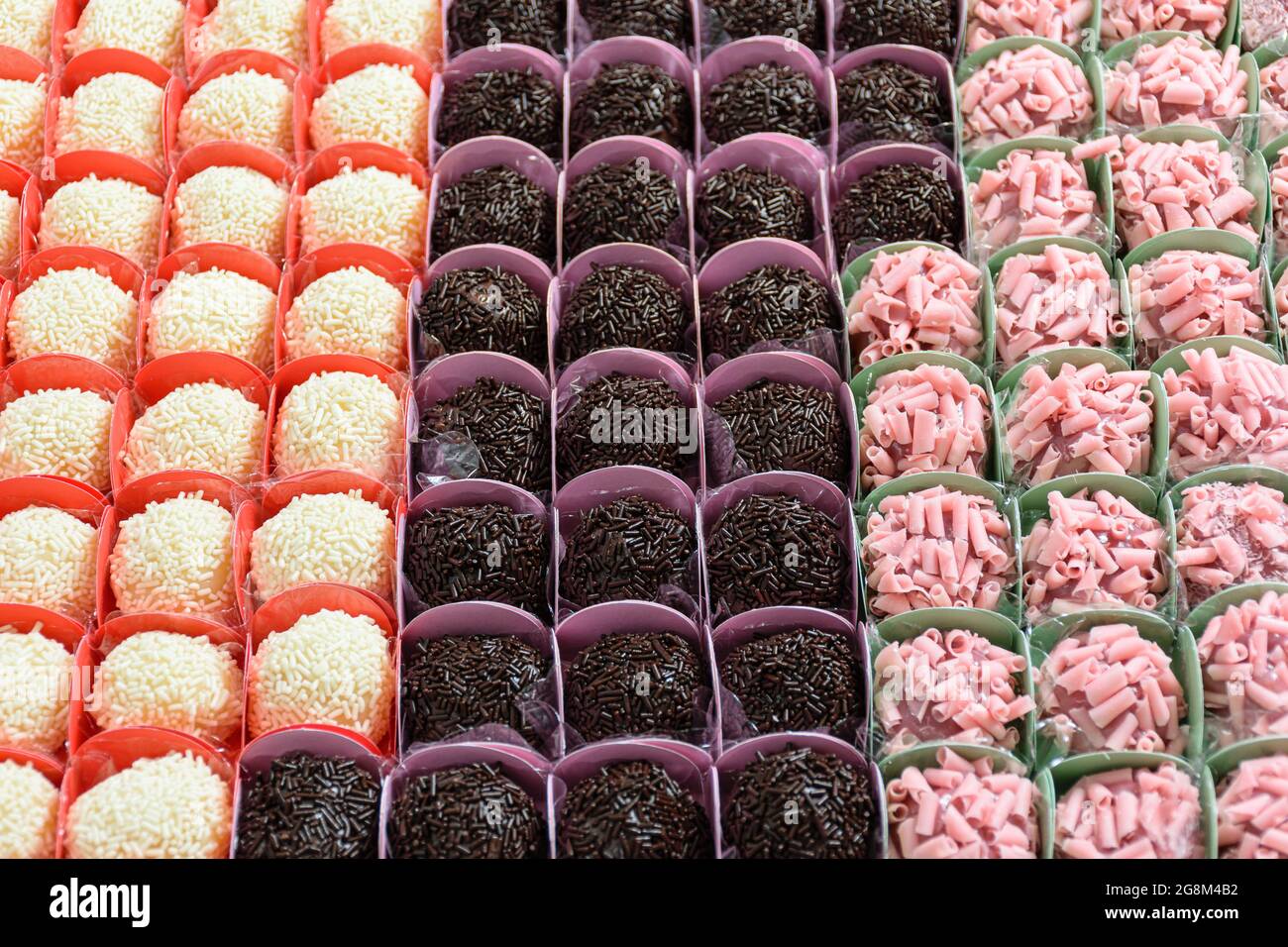 Vari tipi di brigadieri organizzati in file. Brigadieri al cioccolato, alla frutta rossa e al cioccolato bianco. Foto Stock