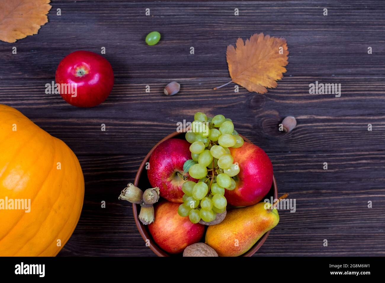 Zucche d'arancia con mele e pere in un cestino con uva, noci e foglie su un tavolo di legno marrone. Vista dall'alto Foto Stock