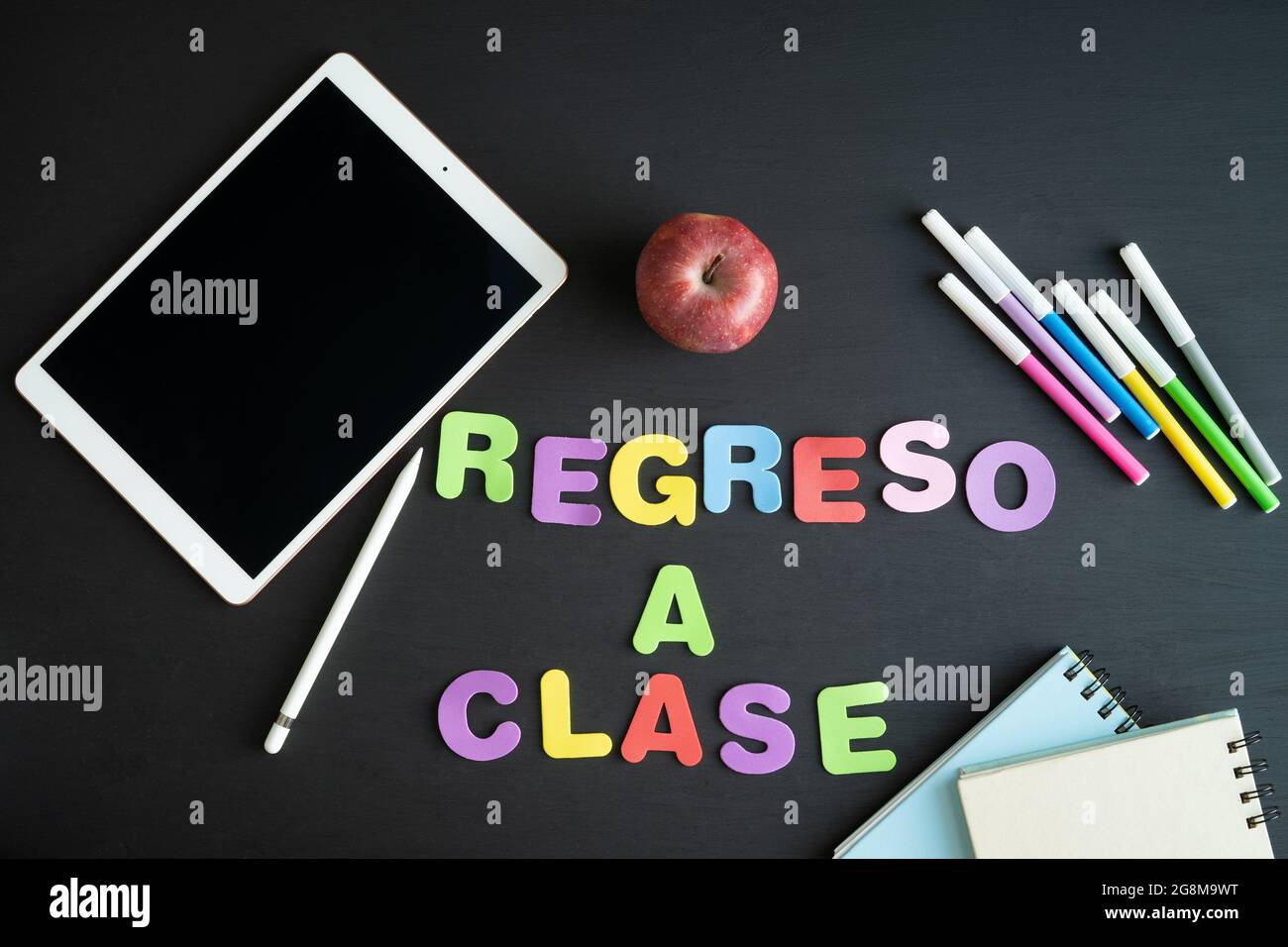 Materiale scolastico con la frase REGRESO A CLASE in spagnolo su sfondo nero. Spazio di copia. Foto Stock