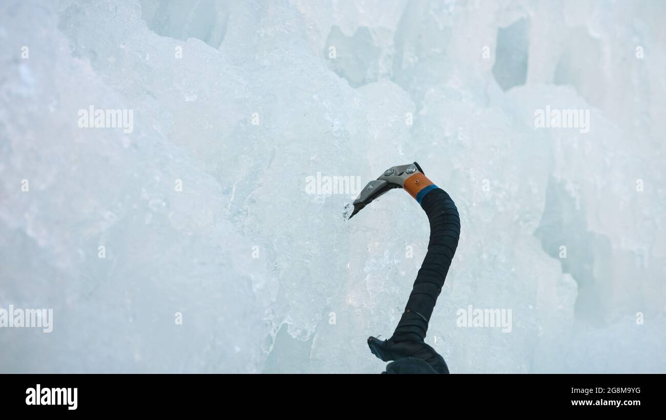 Punto di vista scalatore di ghiaccio che ruota l'ascia di ghiaccio nella superficie verticale coperta di ghiaccio Foto Stock
