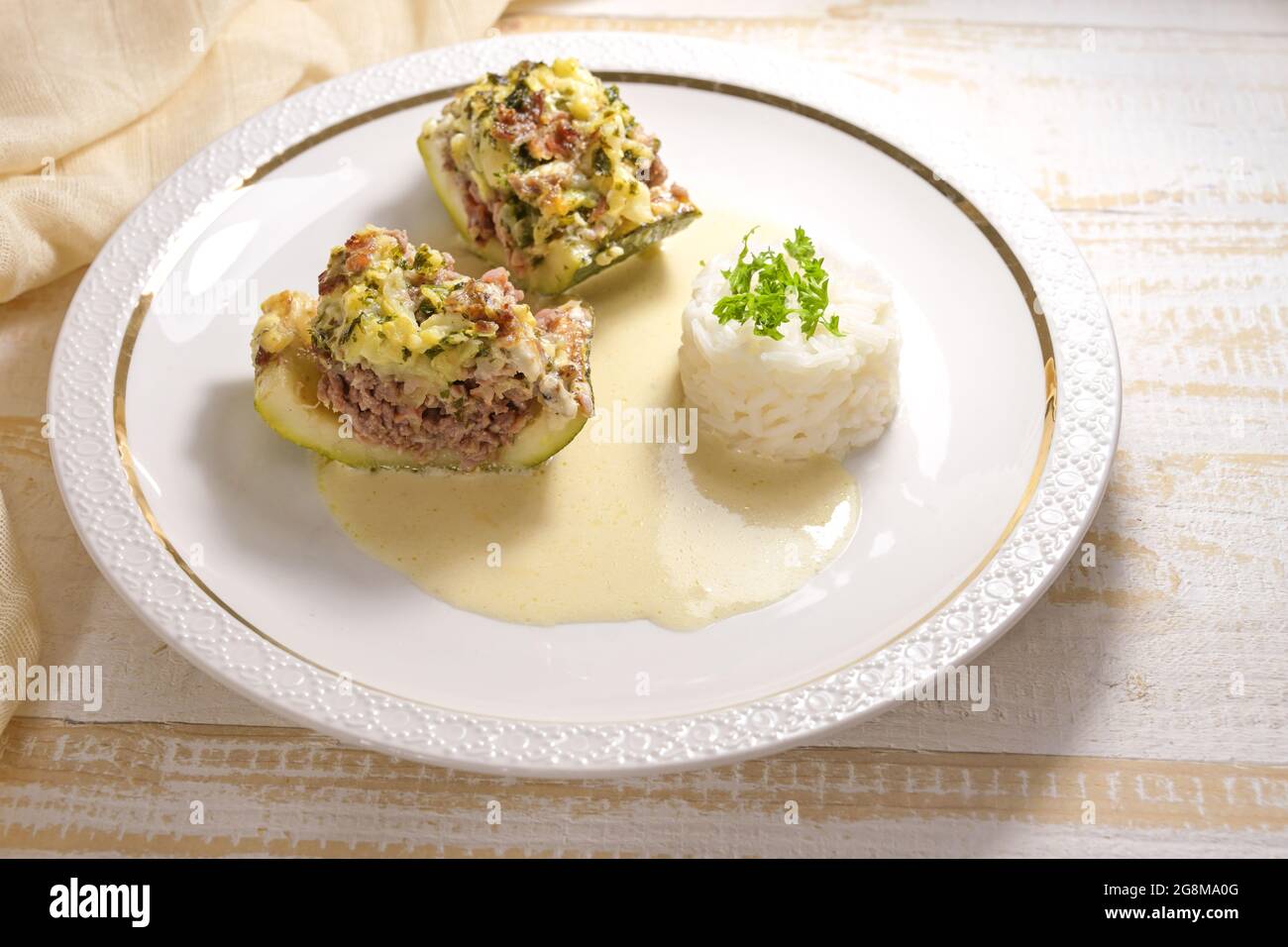 Zucchine o zucchine al forno farcite con manzo tritato, pancetta e panna con riso e salsa al limone su un piatto bianco, fuoco selezionato, profondità ridotta Foto Stock