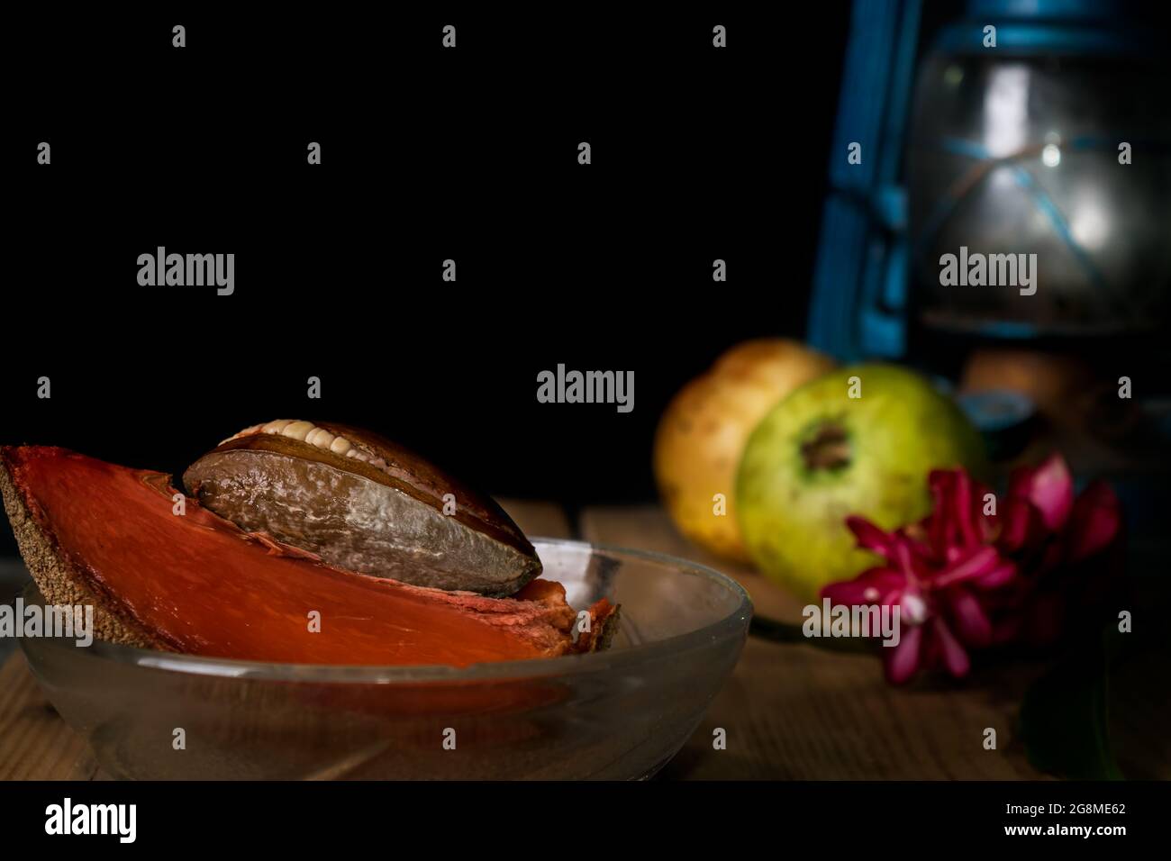 Primo piano di una ciotola di cristallo con una fetta di prugna di saponilla e il suo osso in essa, ci sono anche guava, fiori e una vecchia lanterna fuori fuoco al ri Foto Stock
