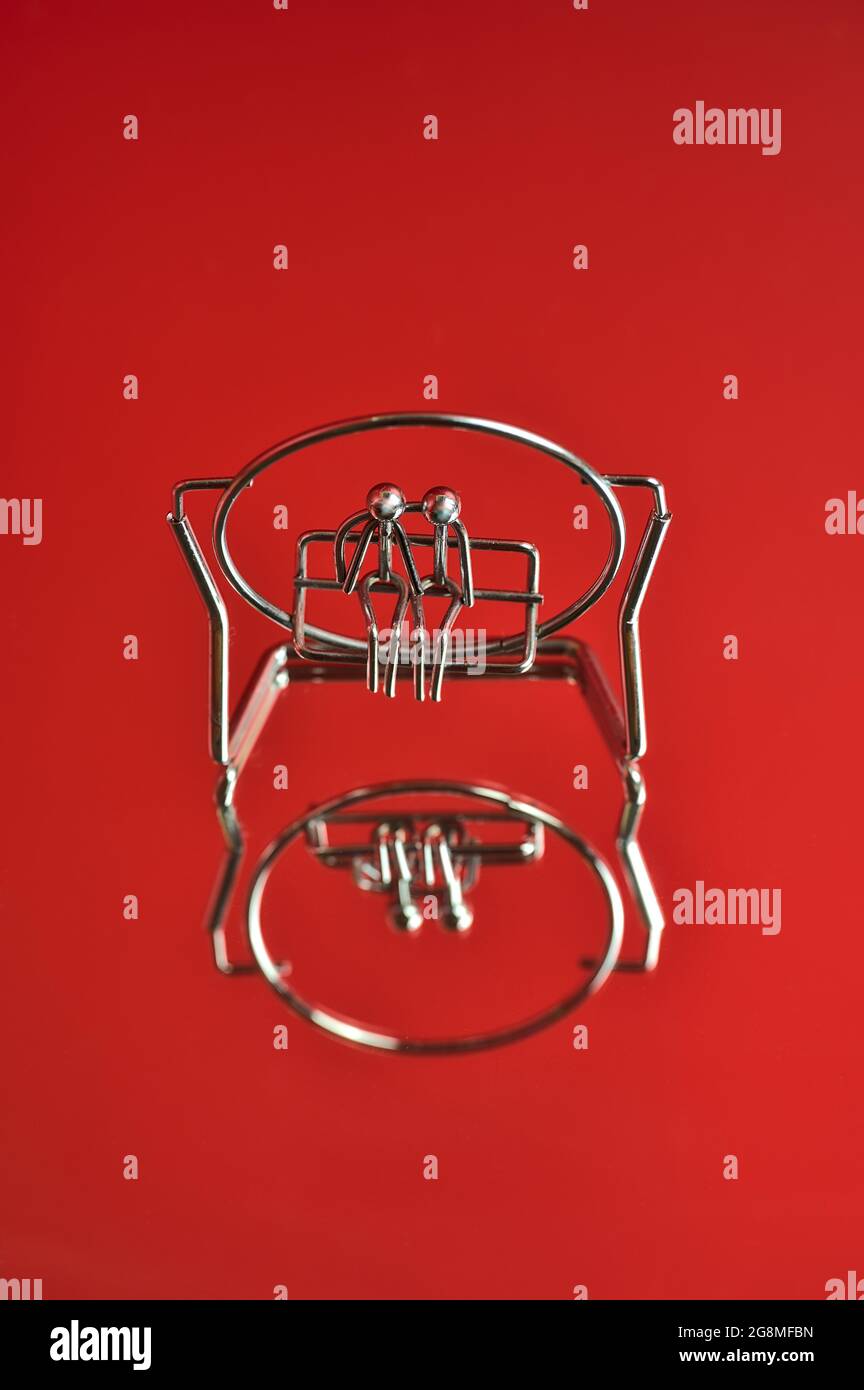 Bella vista closeup di metallo ricordo di coppia seduta su una panca o swing su sfondo rosso riflettente. Amore e affetto concetto. Spazio di copia Foto Stock