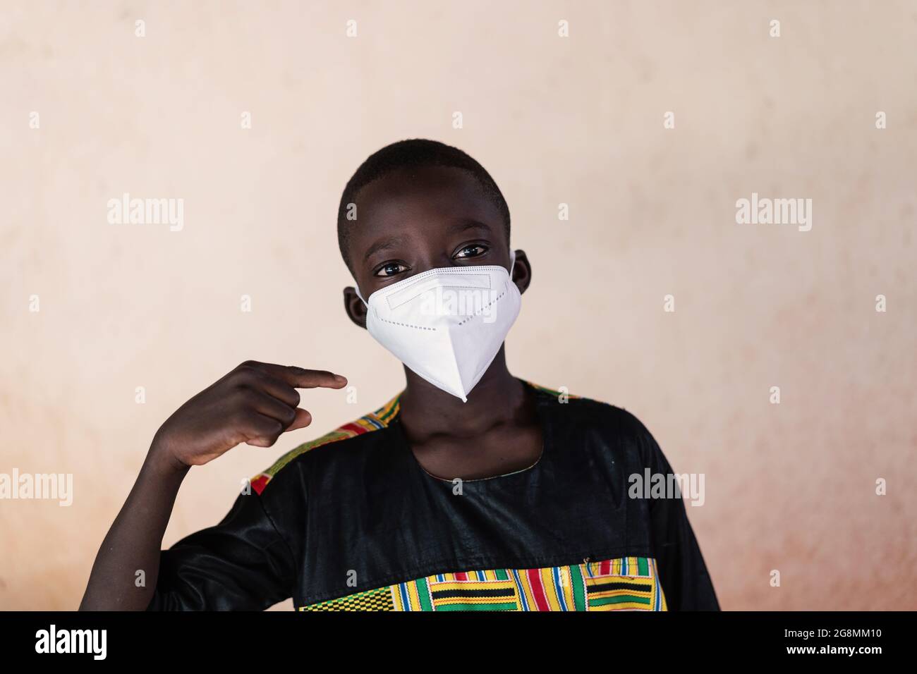 Questa è un'immagine di un piccolo ragazzo africano che guarda la macchina fotografica e punta il dito verso la sua maschera che indossa per proteggersi Foto Stock