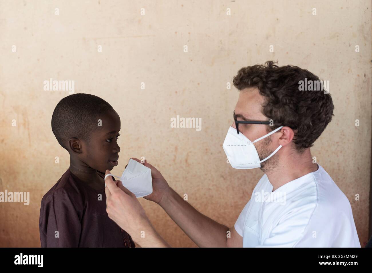 Infermiere caucasico volontariato in Africa aiutare il bambino nero mettendo su una maschera di sicurezza. Questo per prevenire la diffusione di virus mortali. Foto Stock