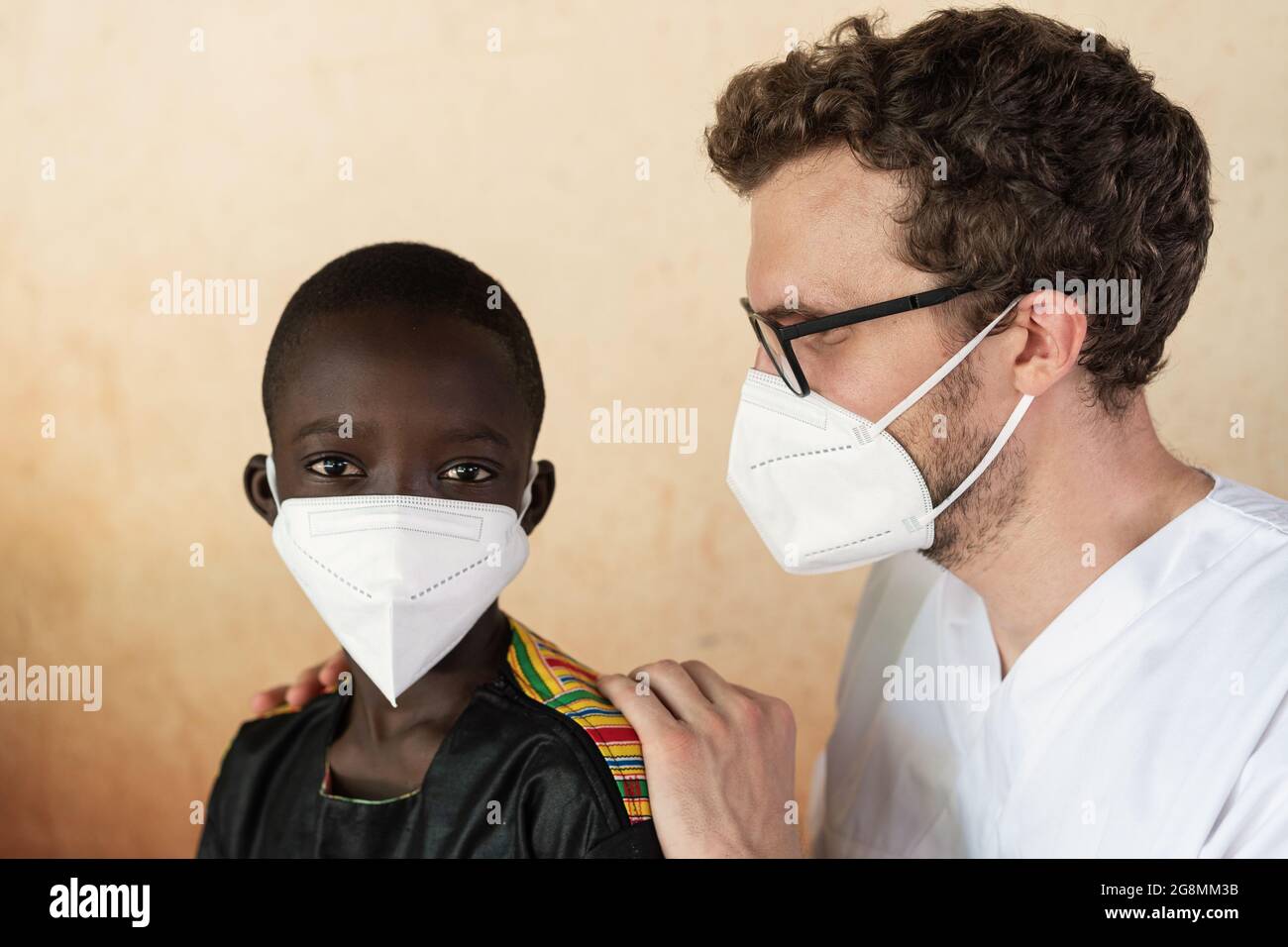 Questa è un'immagine di un'infermiera caucasica bianca che aiuta e assiste un bambino africano nero con maschere facciali per prevenire la diffusione di una malattia pandemica Foto Stock