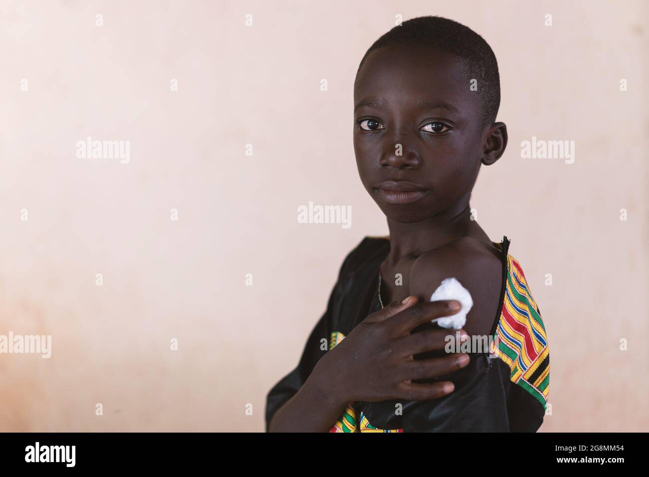 Questa è un'immagine di un bambino africano di etnia nera che mostra orgogliosamente il suo braccio con un bendaggio di cotone dopo aver ottenuto un vaccino colpo. Foto Stock