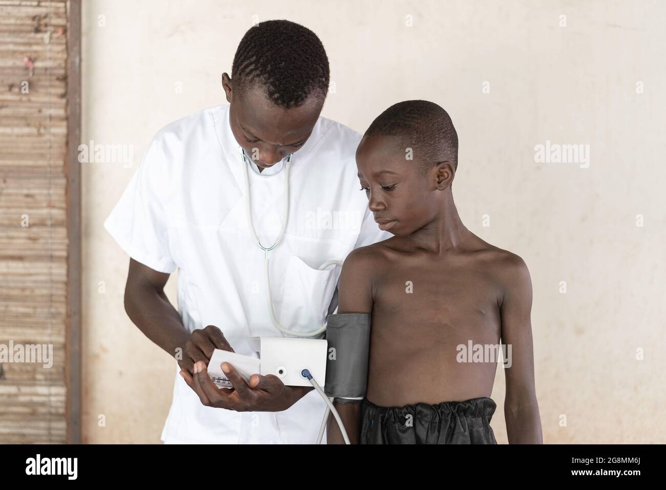 Questa è un'immagine di un infermiere africano di sesso maschile che lavora in un ospedale con uno sfigmomanometro. Un bambino nero sta ottenendo la sua pressione sanguigna misurata. Foto Stock