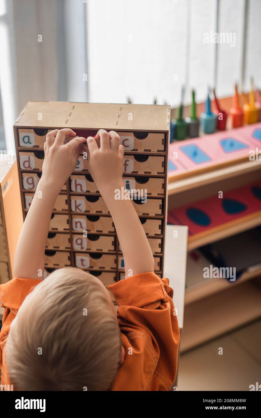 vista posteriore dell'alfabeto di apprendimento del ragazzo mentre si gioca a un gioco educativo nella scuola di montessori Foto Stock