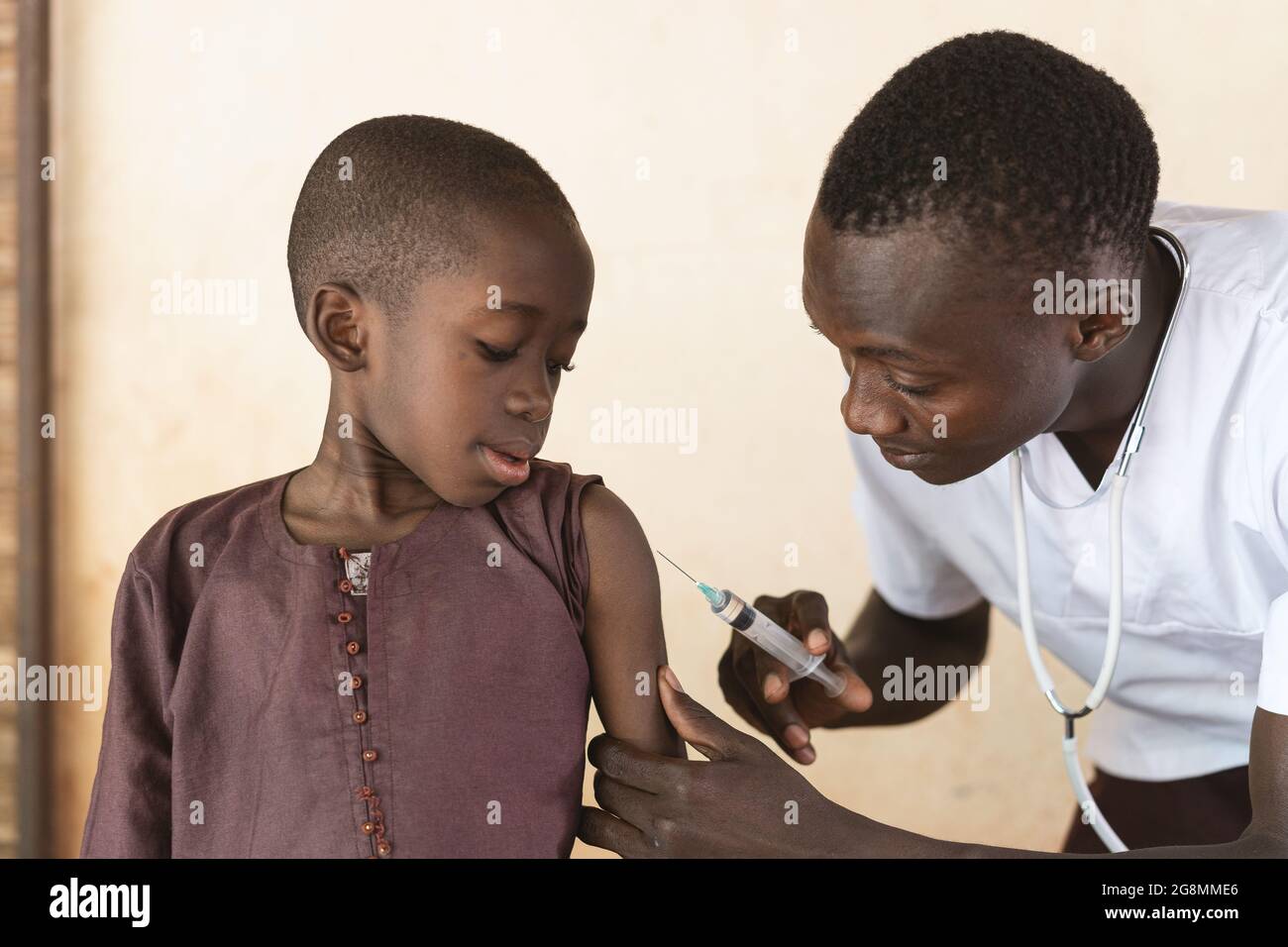 Questa è un'immagine di un carino ragazzo nero africano che ottiene il suo primo vaccino girato nella sua spalla da un medico africano maschio. Foto Stock