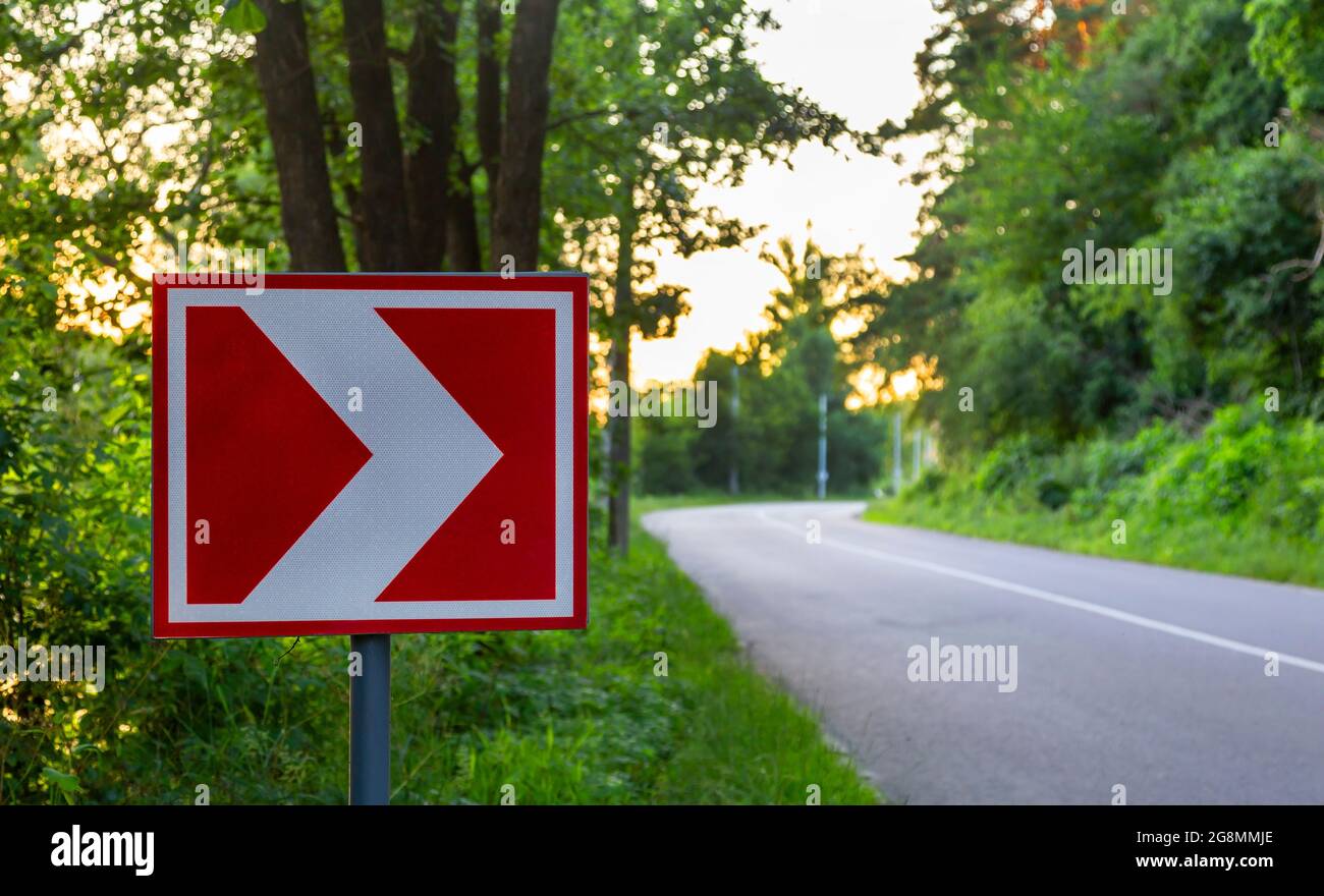 Cartello stradale sulla destra. Puntatore rosso e bianco. Direzione del movimento. Nel mezzo della foresta, primo piano Foto Stock