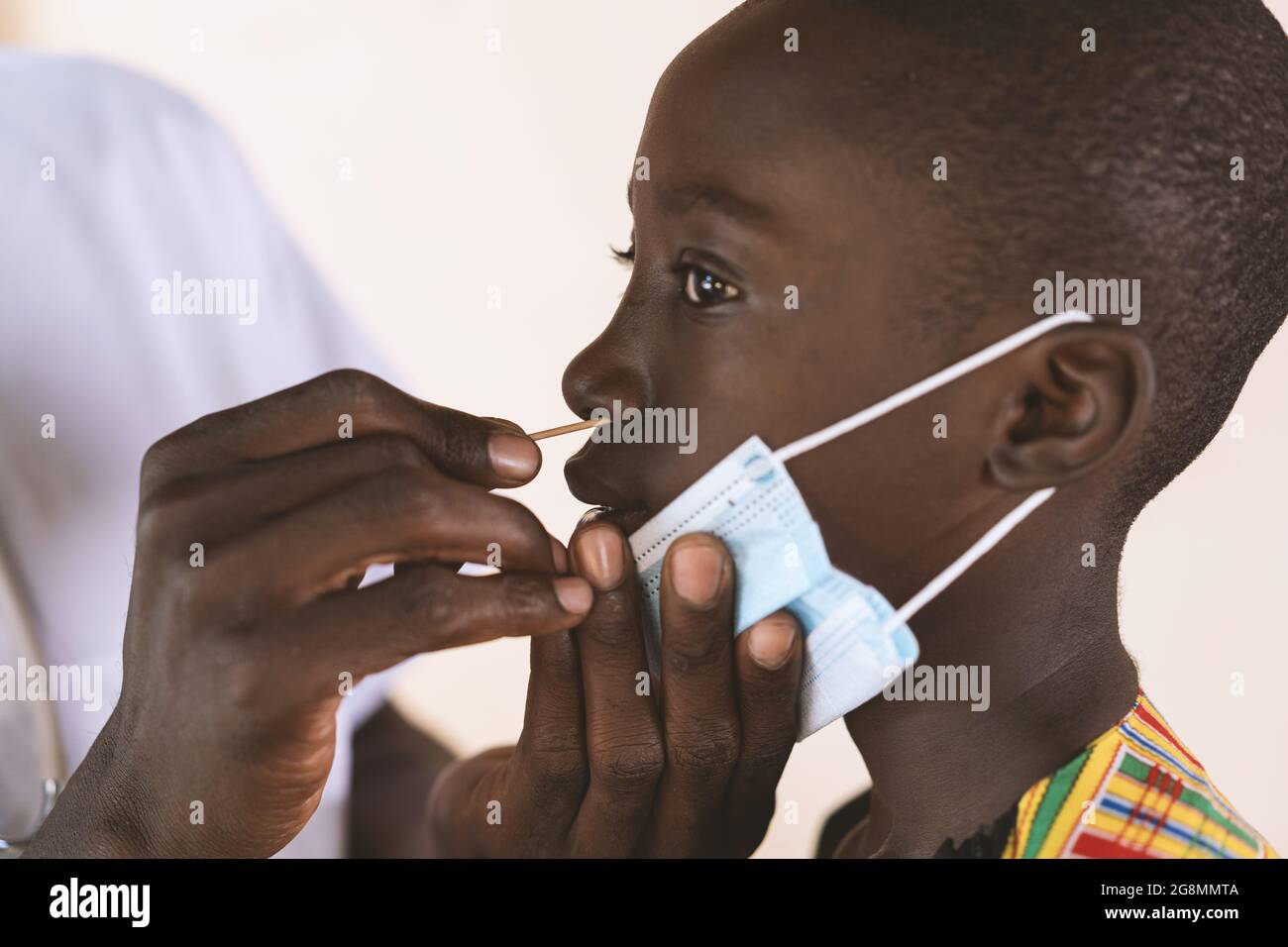 In questa immagine un giovane studente africano con la sua maschera protettiva è testato per il coronavirus da un praticante sanitario nero mettendo un tampone in h Foto Stock