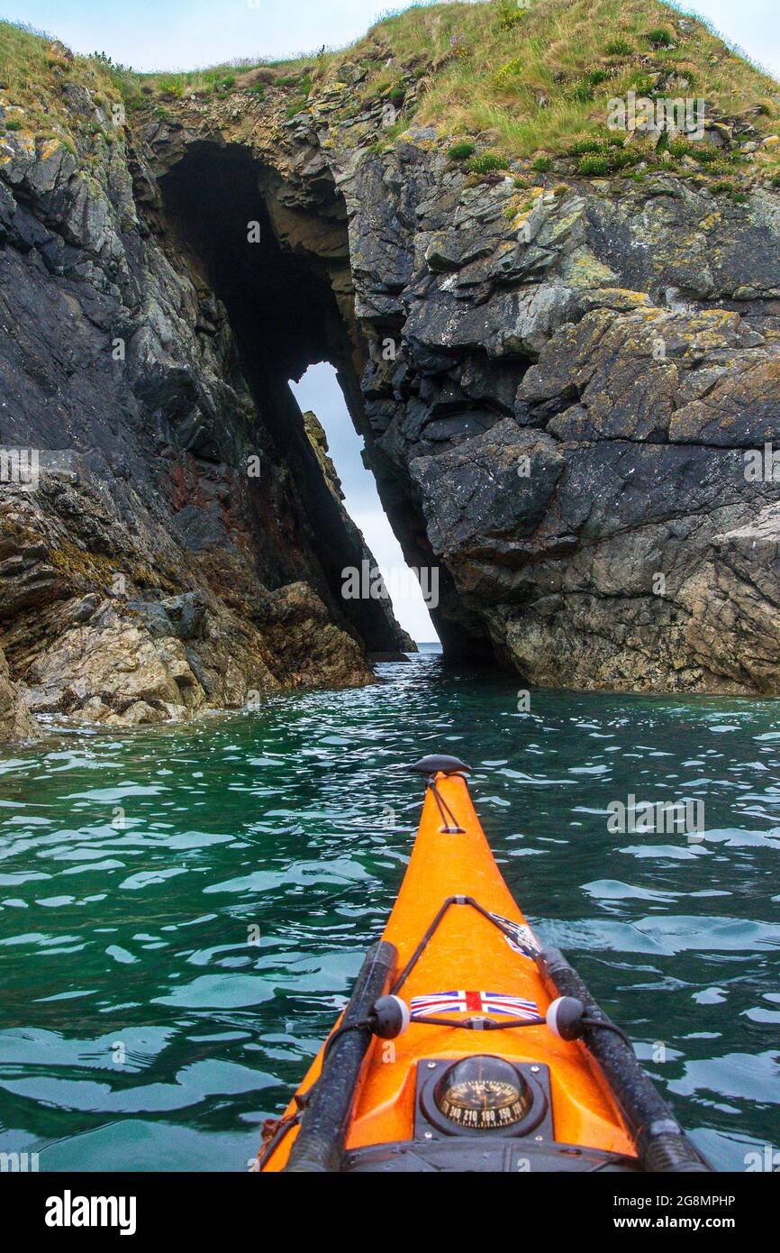 Kayak in mare attraverso una grotta marina sulla costa di Pembrokeshire Foto Stock