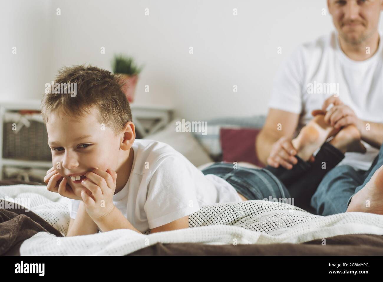 Padre gioca con suo figlio 7-10 a letto. Papà solletico i piedi dei bambini. Divertimento per tutta la famiglia Foto Stock