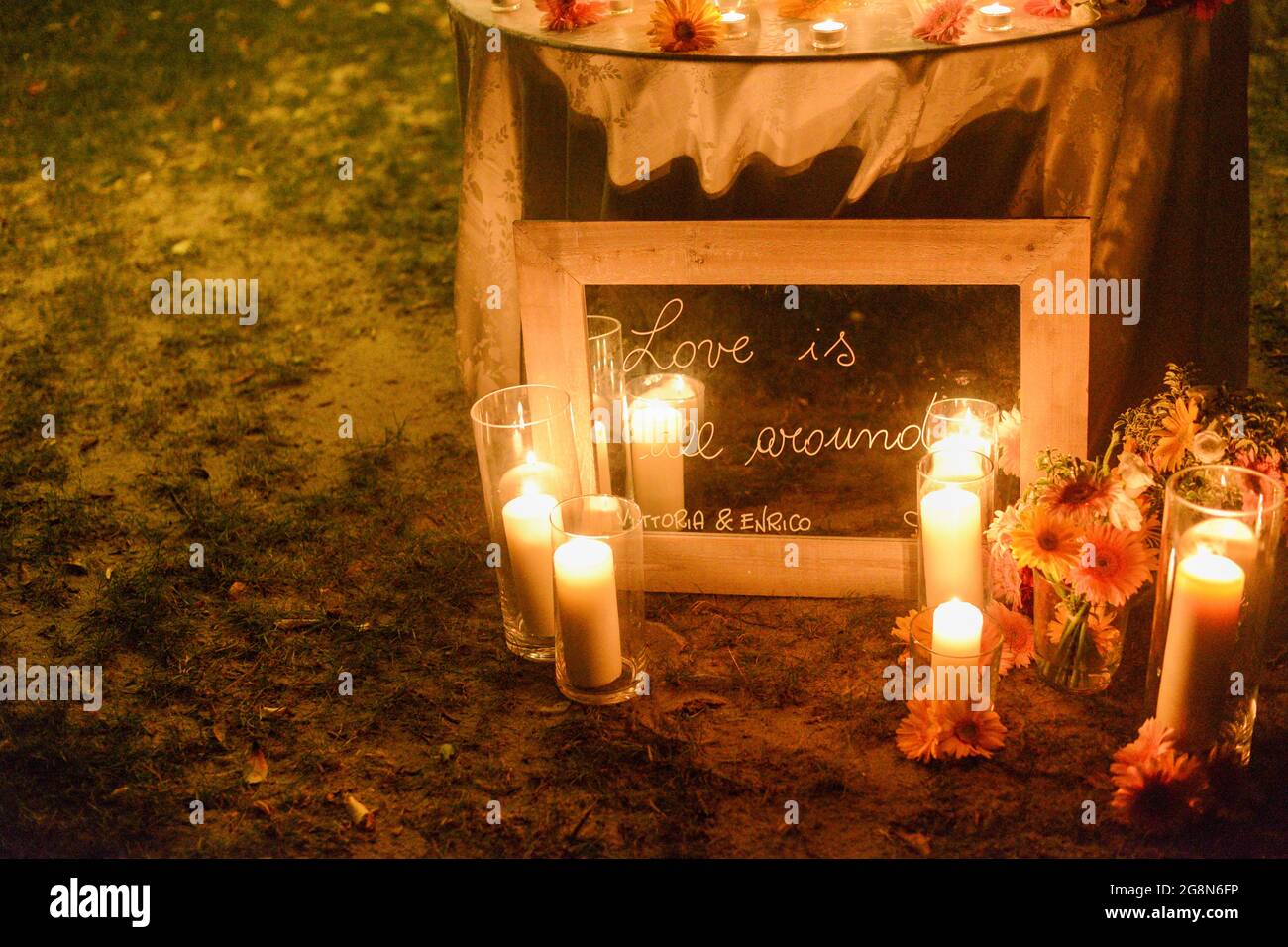 Cornice in legno su una citazione che dice 'l'amore è tutto intorno' con candele luminose a terra di notte Foto Stock