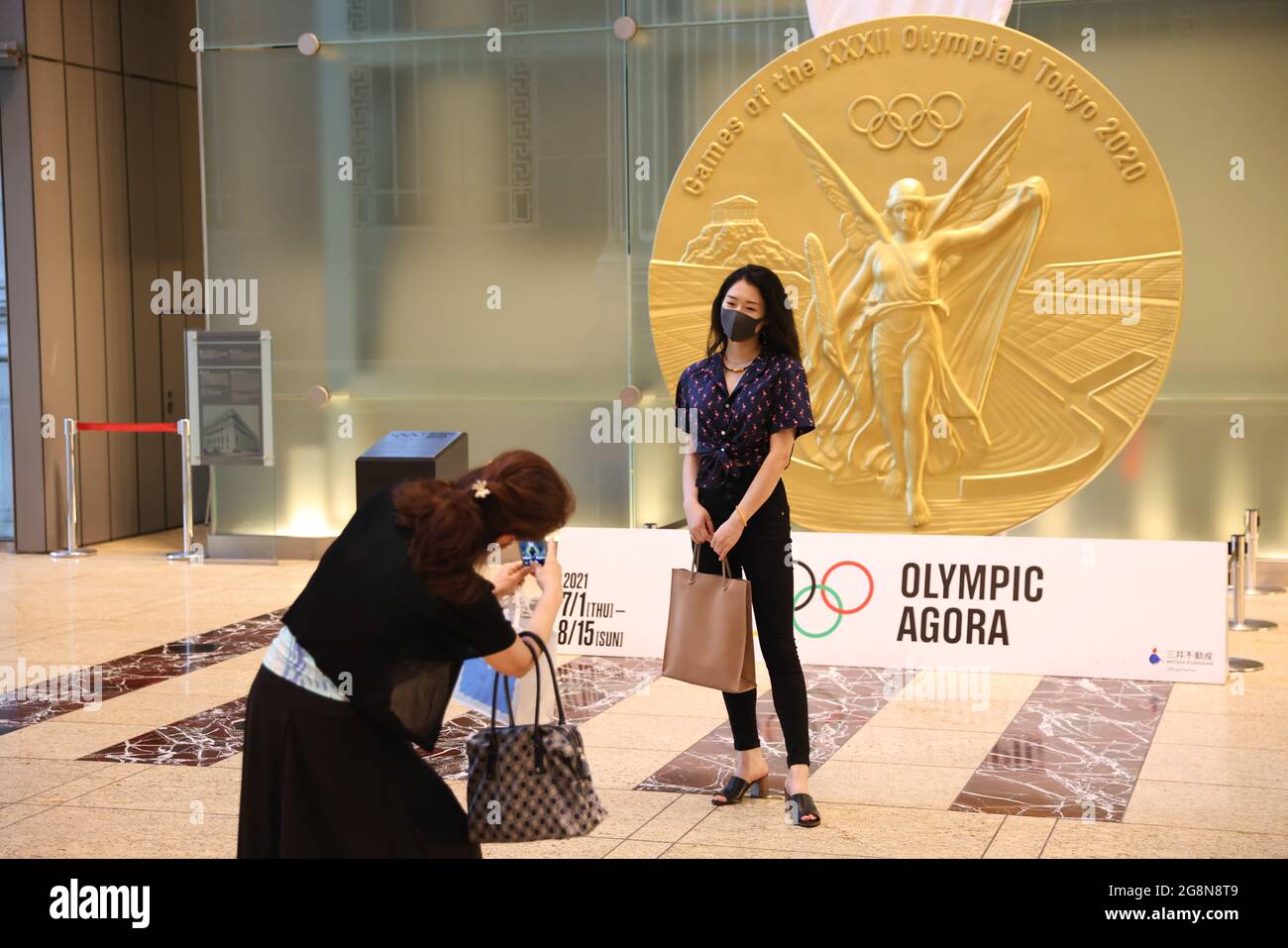Tokyo, Giappone. 21 luglio 2021. Una donna che indossa una maschera posa per una foto di fronte ad una riproduzione su larga scala della medaglia d'oro di Tokyo 2020 in mostra all'Olympic Agora. L'Olympic Agora nel distretto di Nihonbashi è un progetto d'arte che rivive un'antica idea greca di confluenza dello sport, dell'arte e della cultura. 'Agora' viene dal greco e rappresenta uno spazio pubblico vibrante dove le persone si riunivano per acquistare e vendere beni, scambiare idee politiche e fare sport. Credit: SOPA Images Limited/Alamy Live News Foto Stock