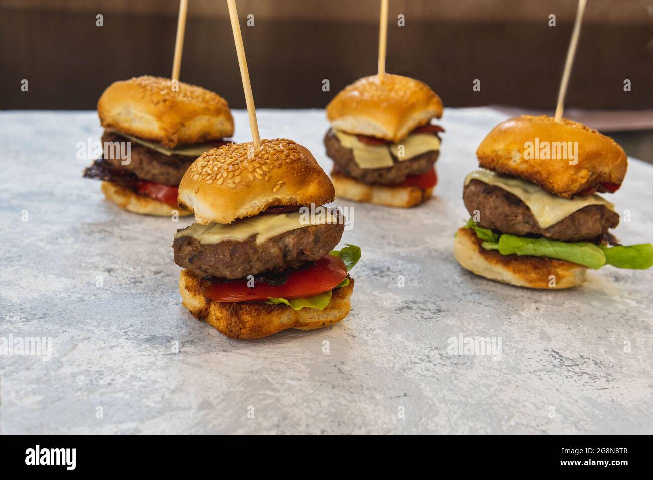 Colpo orizzontale di quattro mini hamburger con formaggio, lattuga, pomodoro e pancetta su un tavolo. Fuoco selettivo di uno degli hamburger Foto Stock