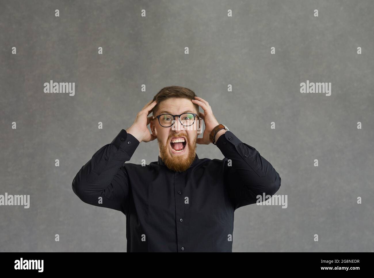 Uomo stressato che tocca la testa e urla in piedi su sfondo grigio studio Foto Stock