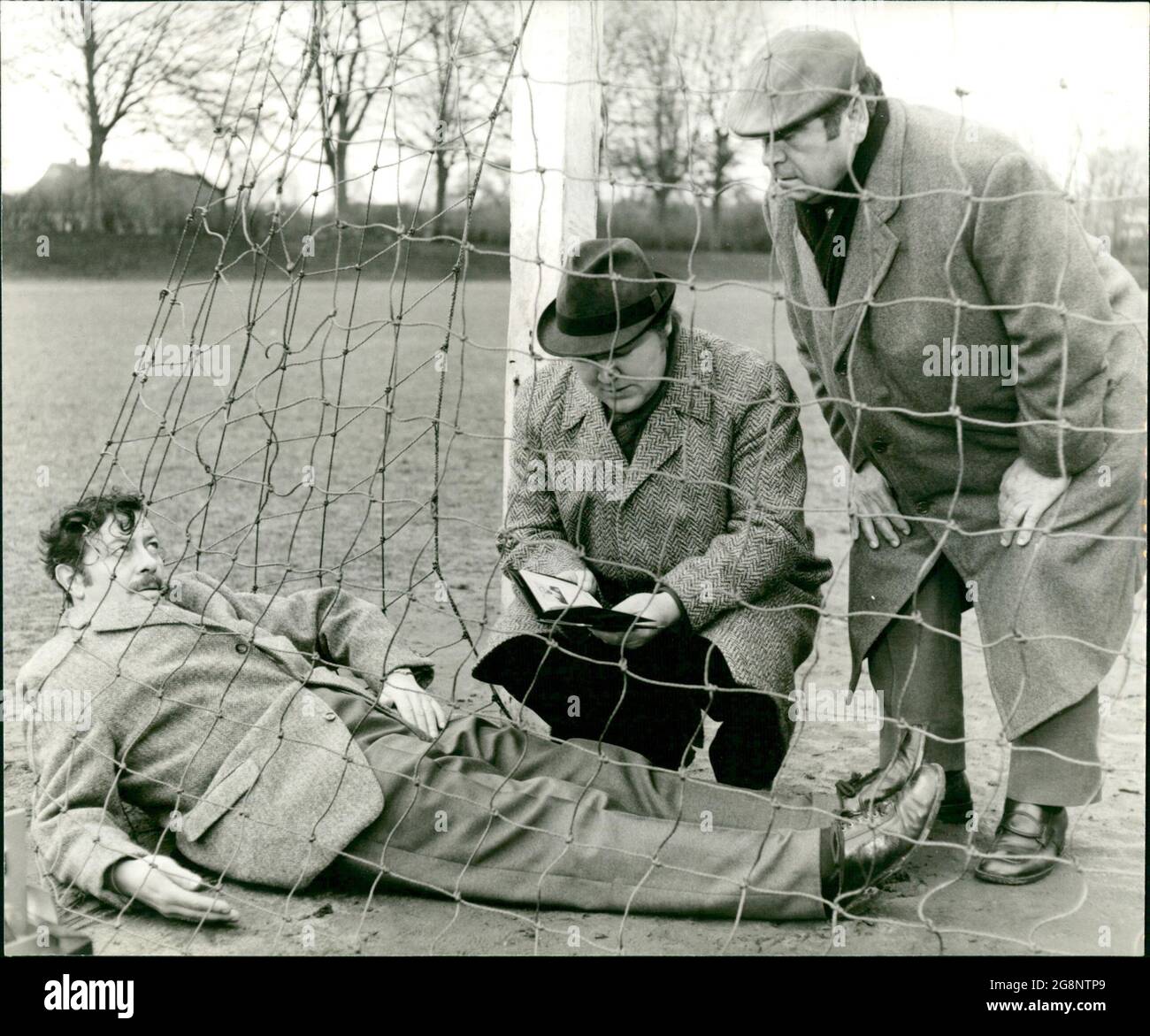 Eines morgens wird die Kripo zum Fußballplatz gerufen. Im Tor Liegt ein Toter (H.G. Meier). Kommissar Trimmel (Walter Richter, mit Mütze) und sein Helfer (Edgar Hoppe, mit Hut) können sofort sehen, dass das Fußballtor nicht der Tatort ist. Jemand muss die Leiche hierher geschleppt haben. Foto Stock