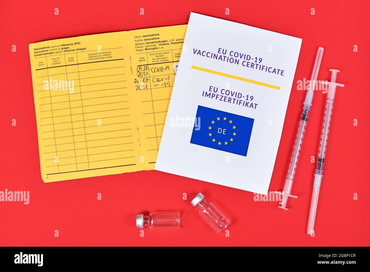 Certificato di vaccinazione EU COVID-19 su carta, passaporto del vaccino e siringhe con flaconcini su sfondo rosso Foto Stock