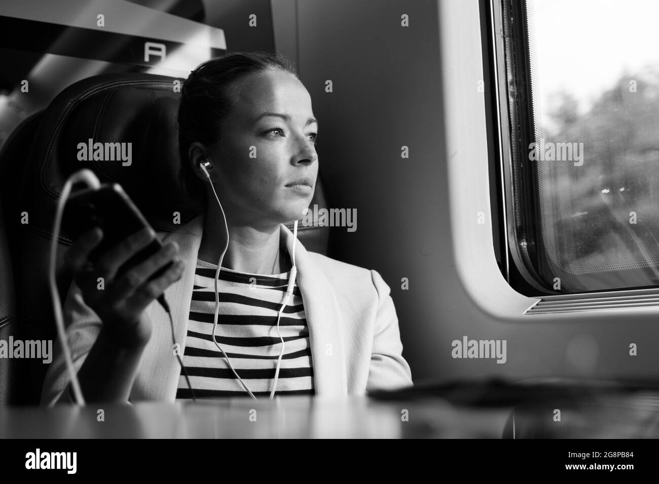 Riflessivo imprenditrice ascolto di podcast sul telefono cellulare mentre si è in viaggio in treno. Foto Stock
