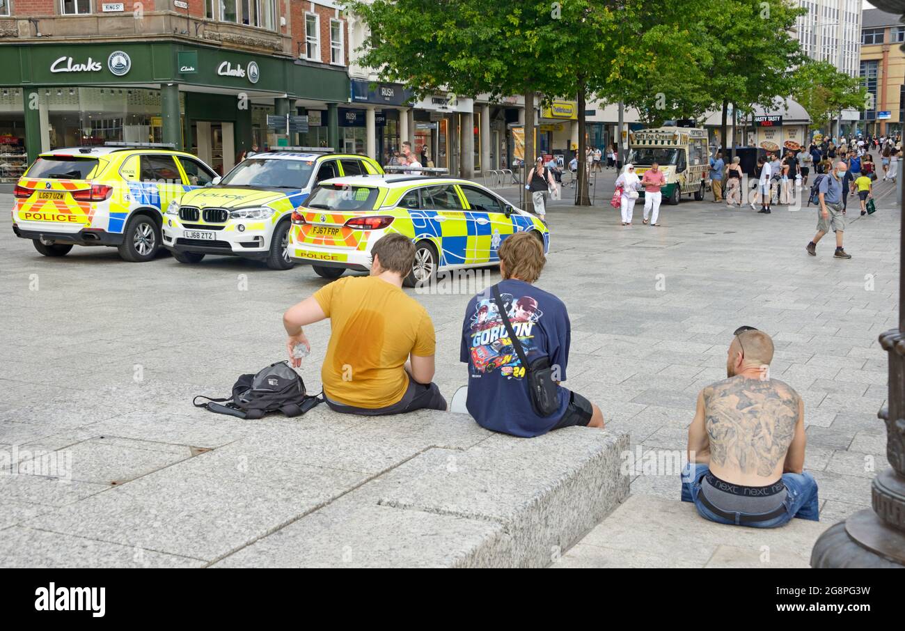 Uomo tatuato e due giovani seduti a guardare l'attività della polizia. Foto Stock
