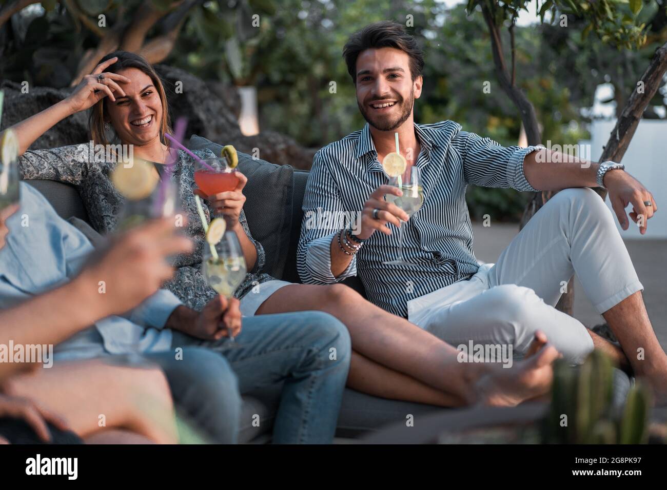 Incontro di giovani che si divertono in un cocktail party seduto su un divano in una terrazza. Amici che celebrano il concetto di stile di vita. Foto Stock