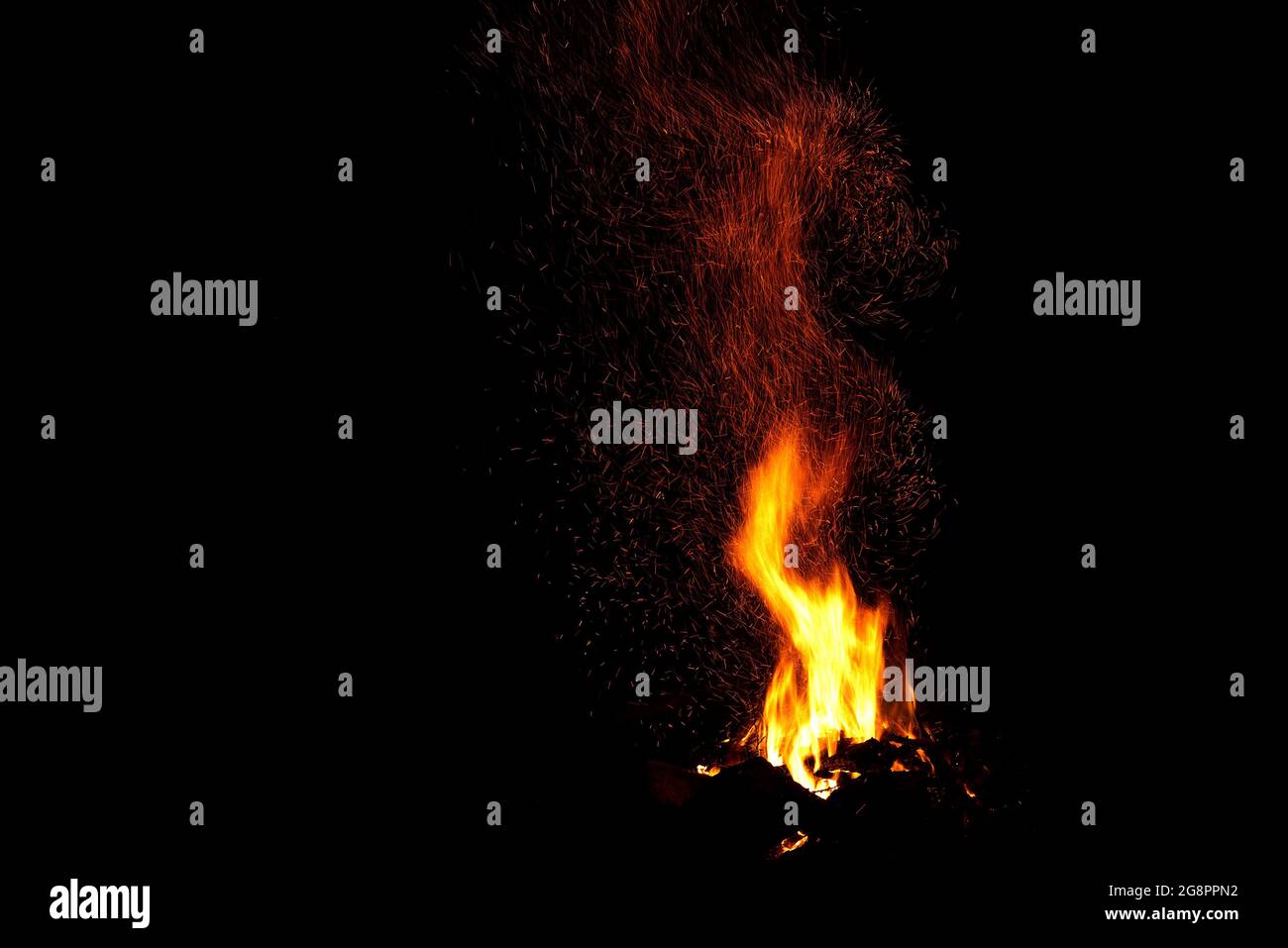 Incredibile falò con belle fiamme gialle e arancioni e un enorme fascio di scintille sotto forma di tracce su sfondo nero Foto Stock