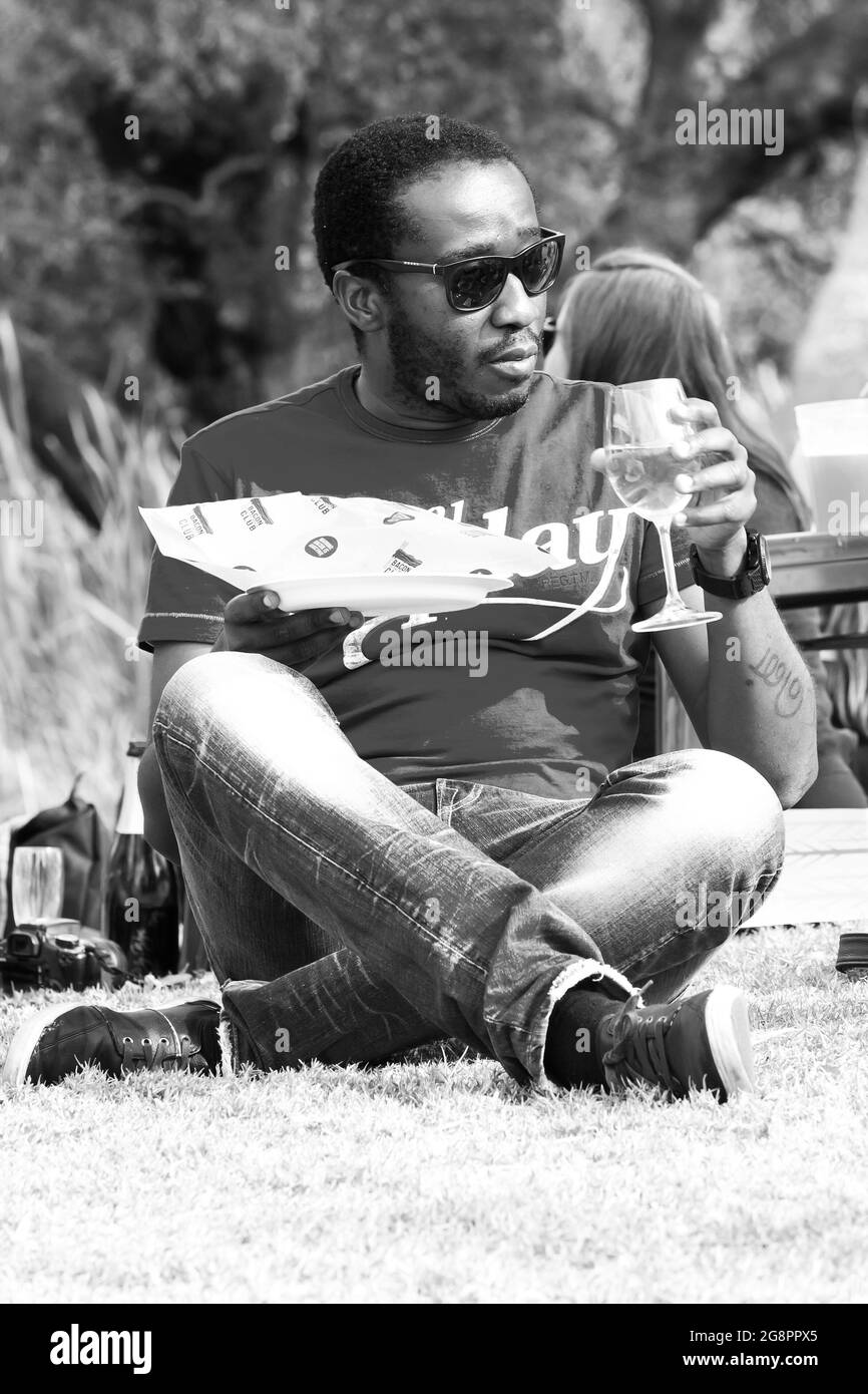 Uomo africano seduto sull'erba e bevendo vino in un festival all'aperto di cibo e vino a Johannesburg Foto Stock