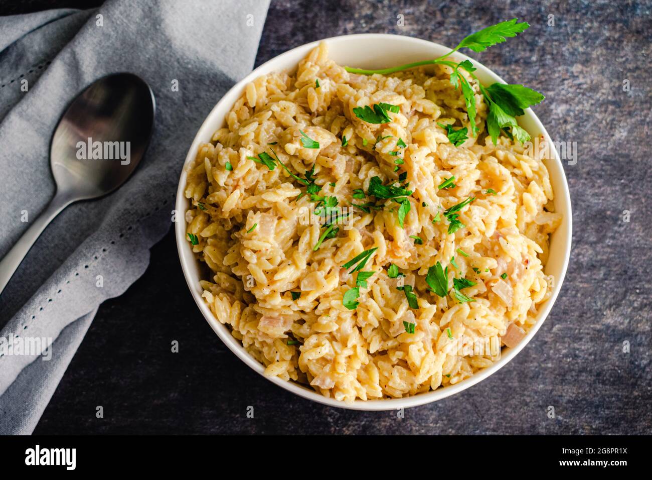 Orzo cremoso di parmigiano guarnito con prezzemolo: Una ciotola di orzo in salsa di parmigiano e crema con contorno di prezzemolo Foto Stock