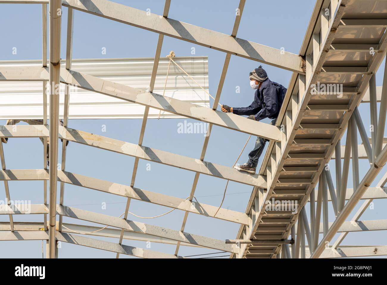 Uomo che lavora su lamiera per tetti su truss in acciaio leggero e costruzione di telai. Foto Stock