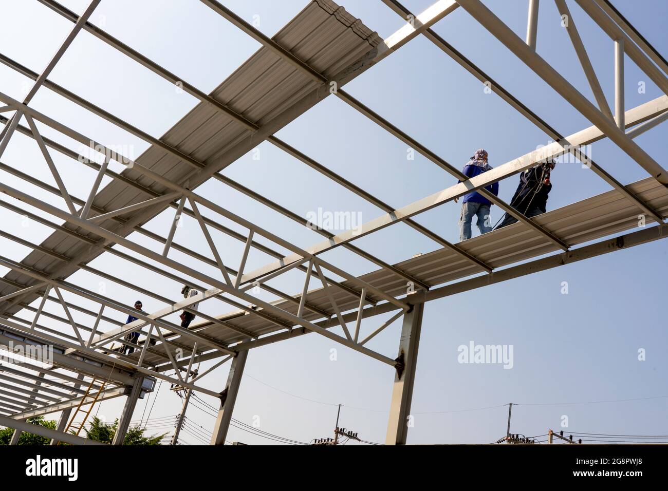 Tre uomini stanno installando la lamiera del tetto su truss di acciaio leggero e costruzione del telaio. Foto Stock