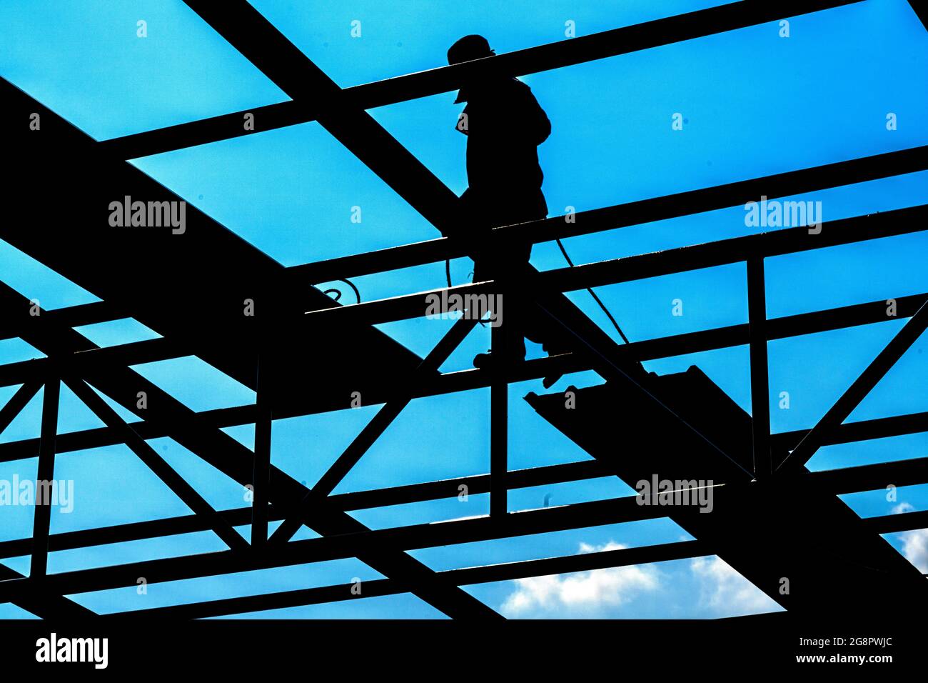 Un uomo sta installando la lamiera del tetto su truss di acciaio leggero e costruzione del telaio. Foto Stock