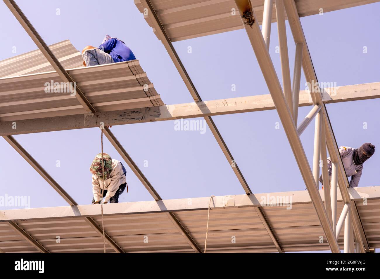 Tre uomini stanno installando la lamiera del tetto su truss di acciaio leggero e costruzione del telaio. Foto Stock