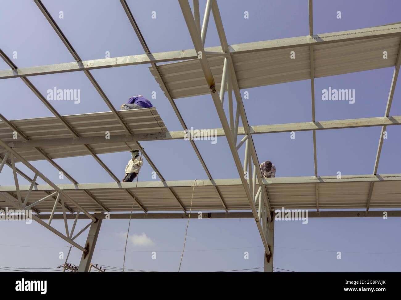 Tre uomini stanno installando la lamiera del tetto su truss di acciaio leggero e costruzione del telaio. Foto Stock