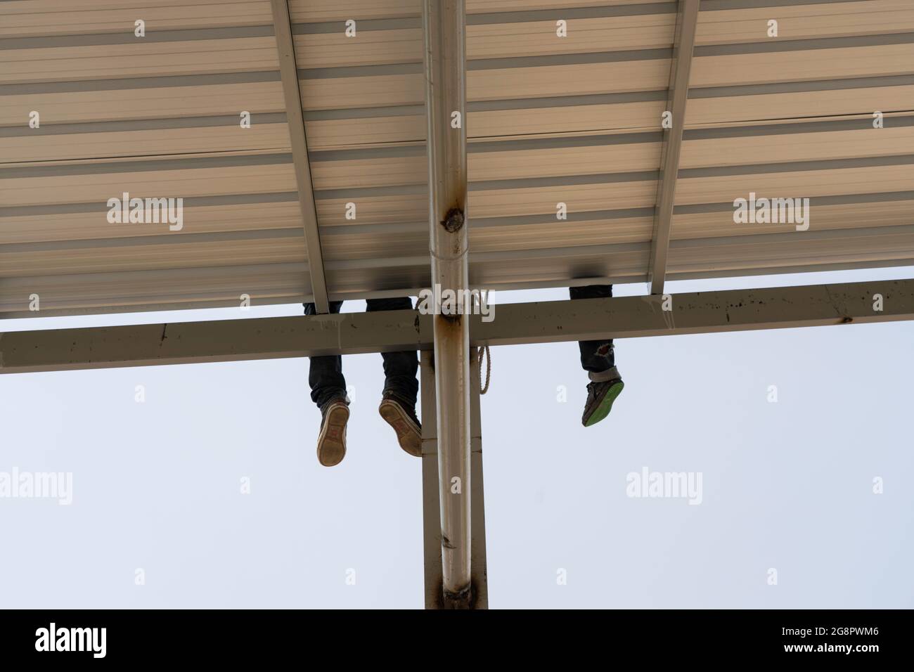 Due gambe di sospensione uomo sulla lamiera del tetto su truss in acciaio leggero e struttura del telaio. Foto Stock