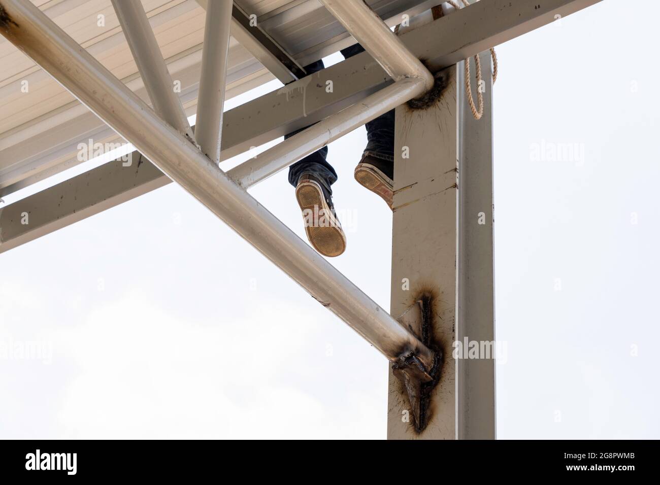 Un uomo stava appeso gamba sulla lamiera del tetto su truss di acciaio leggero e costruzione di telaio. Foto Stock